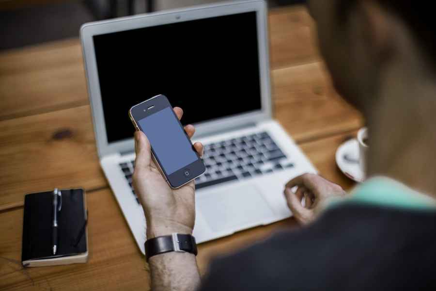 Man with cell phone in hand and laptop computer in background